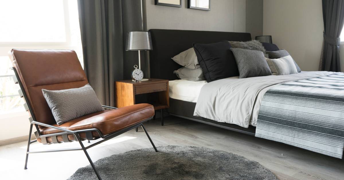 A bedroom with a leather chair that has a pillow on it. The chair is brown, and it's sitting on a gray carpet.