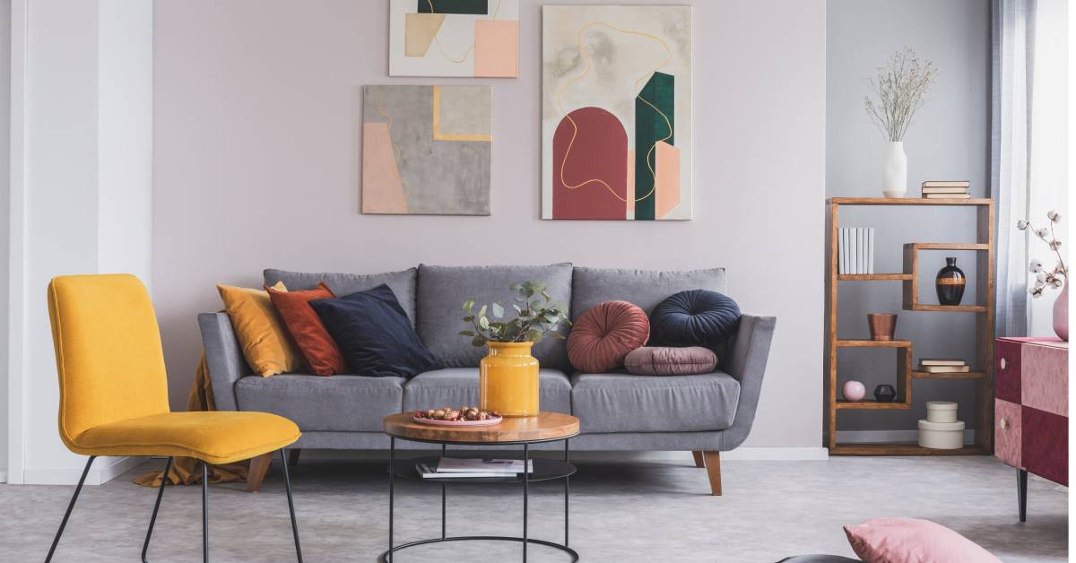 A room with a gray couch, a yellow chair, a small coffee table, and modern abstract art on the wall.