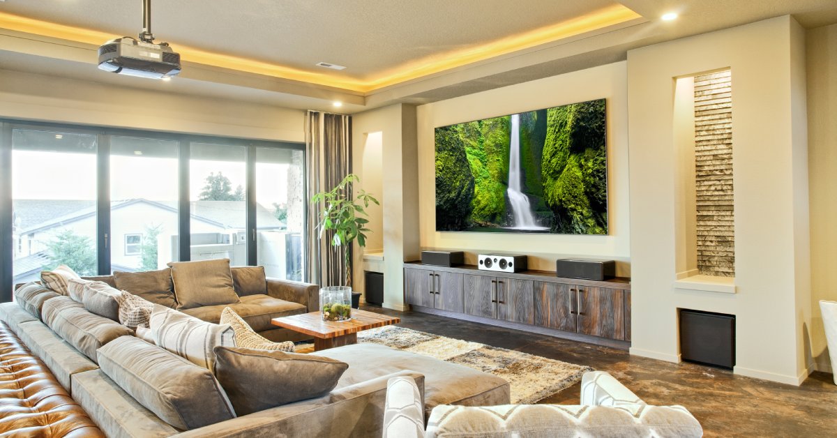 A room with a large couch, speakers, and a flat-screen television. There are also speakers and cabinets in the room.