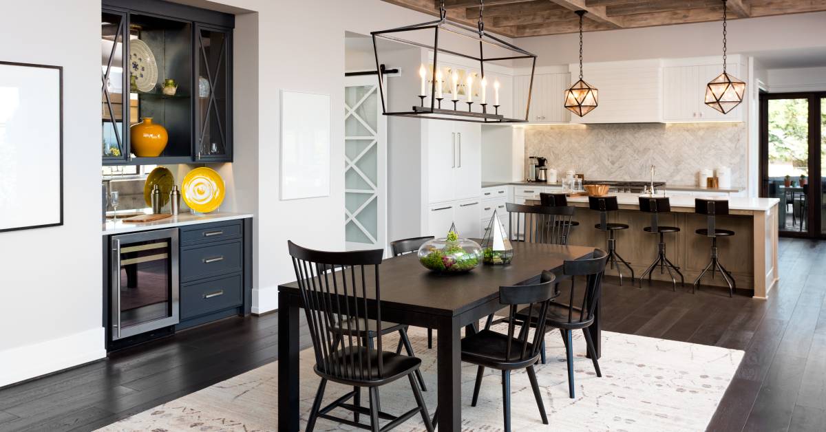 A dark brown dining table with a white rectangular rug. White kitchen cabinets and an island are in the background.