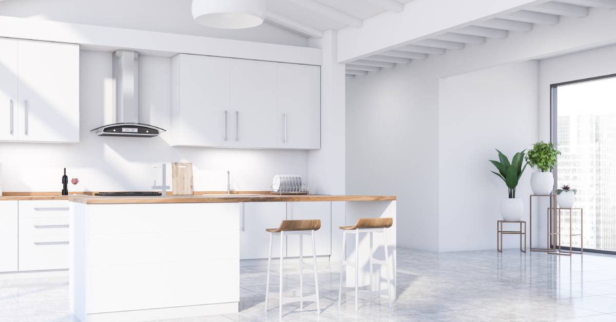 A kitchen area with an island and bar stools. There are also plants and a window in the corner.